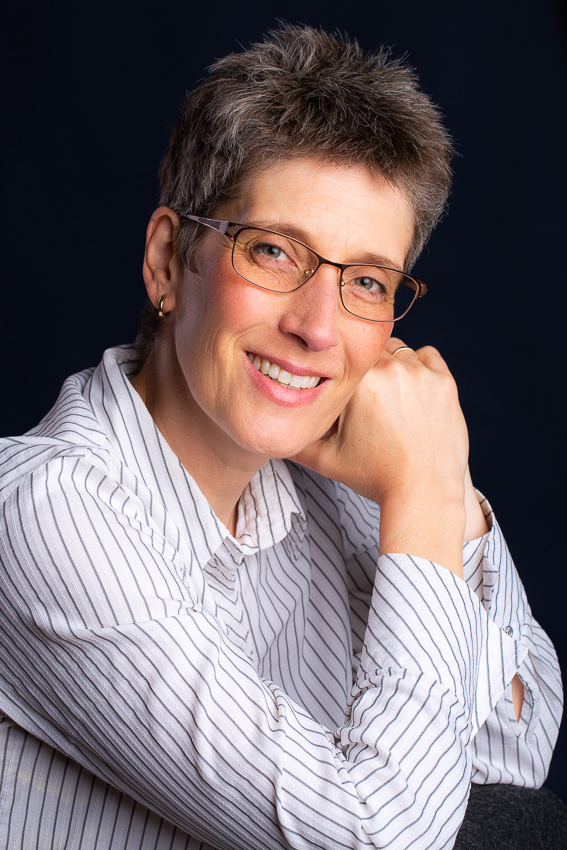 Sabine M. Schröder – Meer Verstehen-Akademie Sabine M. Schröder schaut fröhlich lächelnd schräg in die Kamera. Ihr Kopf ist leicht auf die Hände gestützt, sie trägt eine weiße Bluse mit grauen dünnen Streifen.